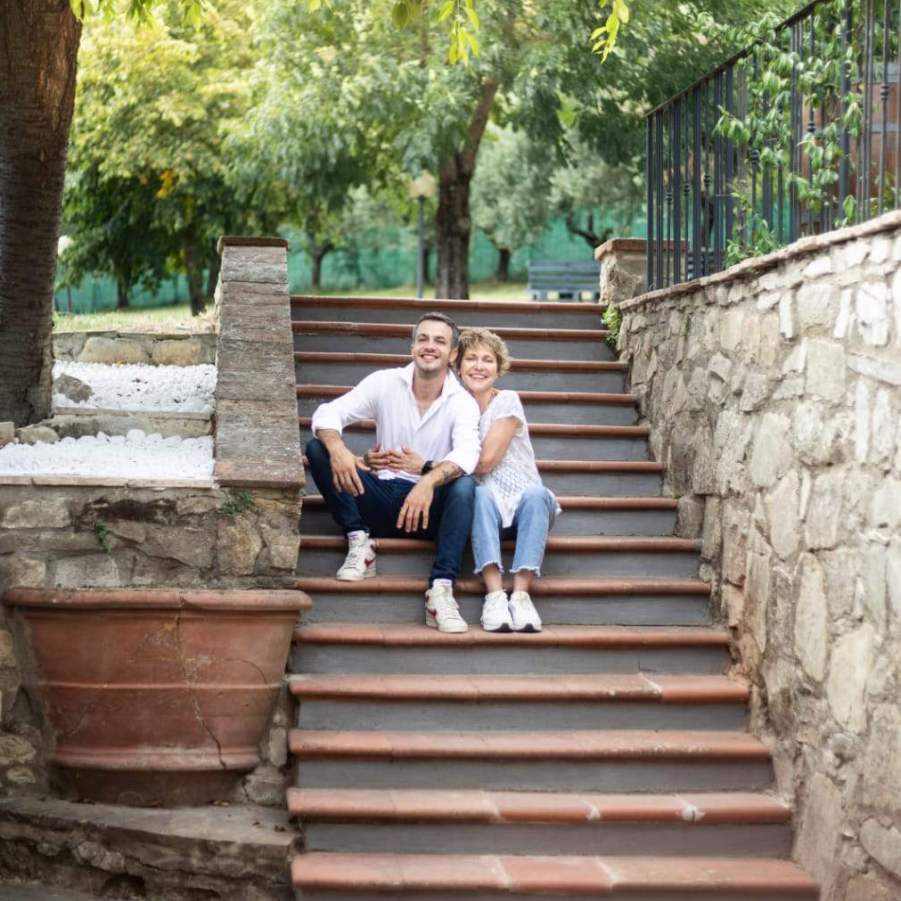 I proprietari dell'agriturismo Tassinaia, madre e figlio, sorridenti mentre posano insieme sulle scale dell'agriturismo.